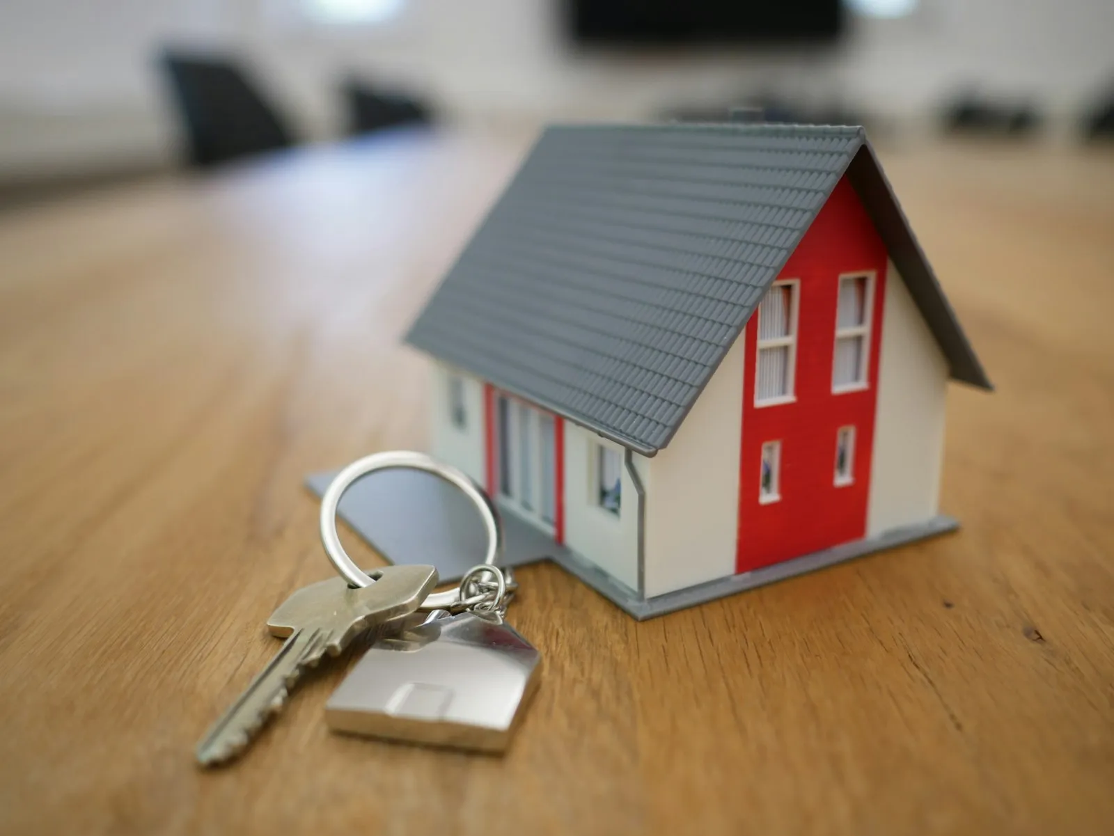Hausschlüssel mit Modellhaus auf einem Holztisch